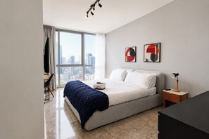 A modern bedroom with a large window, a bed, a bedside table, and a desk with a chair. - Exclusive NEW 1BR with balcony in Yoo Panama (Panamá)