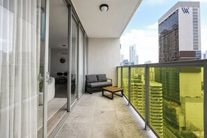 A balcony with a sofa, a small table, and a sliding glass door leading to a dining area. - Exclusive NEW 1BR with balcony in Yoo Panama (Panamá)