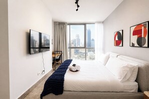 A hotel room with a bed, a desk, a chair, a TV, and a view of the cityscape. - Exclusive NEW 1BR with balcony in Yoo Panama (Panamá)