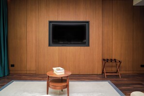 Une chambre moderne avec un mur lambrissé en bois, un grand téléviseur fixé au mur, une petite table ronde en bois sur laquelle repose un livre, et une chaise en bois.