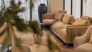 A modern living room with a beige sectional sofa, a small table, and a large vase. - Supreme Hotel (Golem)