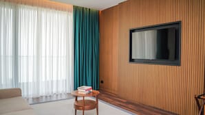Un salon moderne avec un canapé, une petite table en bois sur laquelle sont posés des livres, un téléviseur fixé à un mur en bois et des rideaux légers.