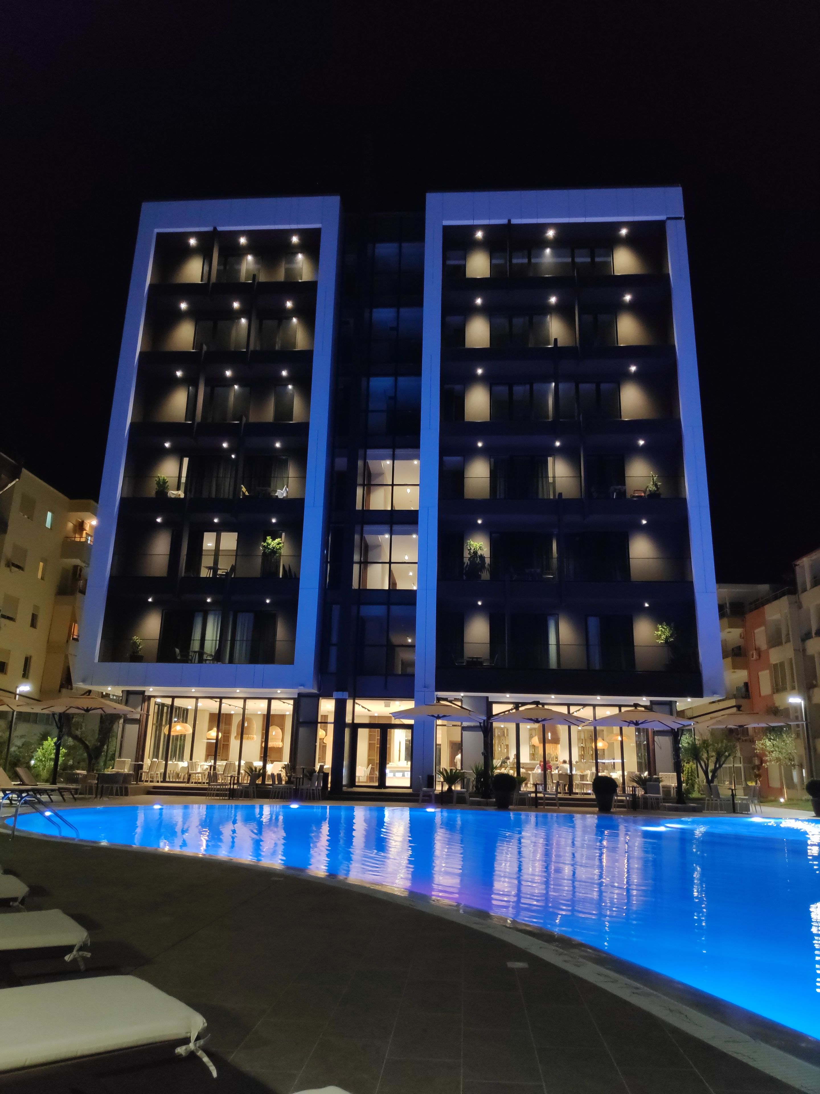 A modern hotel with a pool area, featuring a large outdoor pool and multiple balconies with lighting.