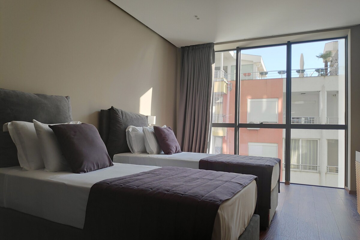 Une chambre d’hôtel avec deux lits, une grande fenêtre et une vue sur le paysage urbain.
