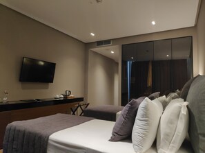 A modern hotel room with a bed, a flat-screen TV mounted on the wall, a small table with a kettle, and a large window with a view of the outside. - Supreme Hotel (Golem)
