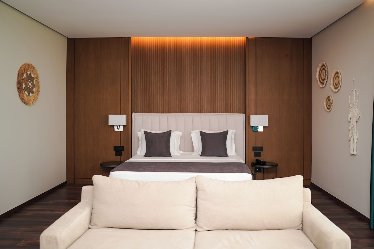 Een moderne slaapkamer met een groot bed, twee nachtkastjes, een bank en decoratieve wandkunst.