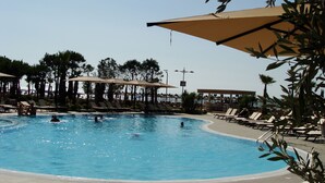 A swimming pool with lounge chairs and umbrellas, surrounded by palm trees. - Supreme Hotel (Golem)
