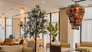 A modern lobby with leather sofas, a large tree, and a unique shell chandelier. - Supreme Hotel (Golem)