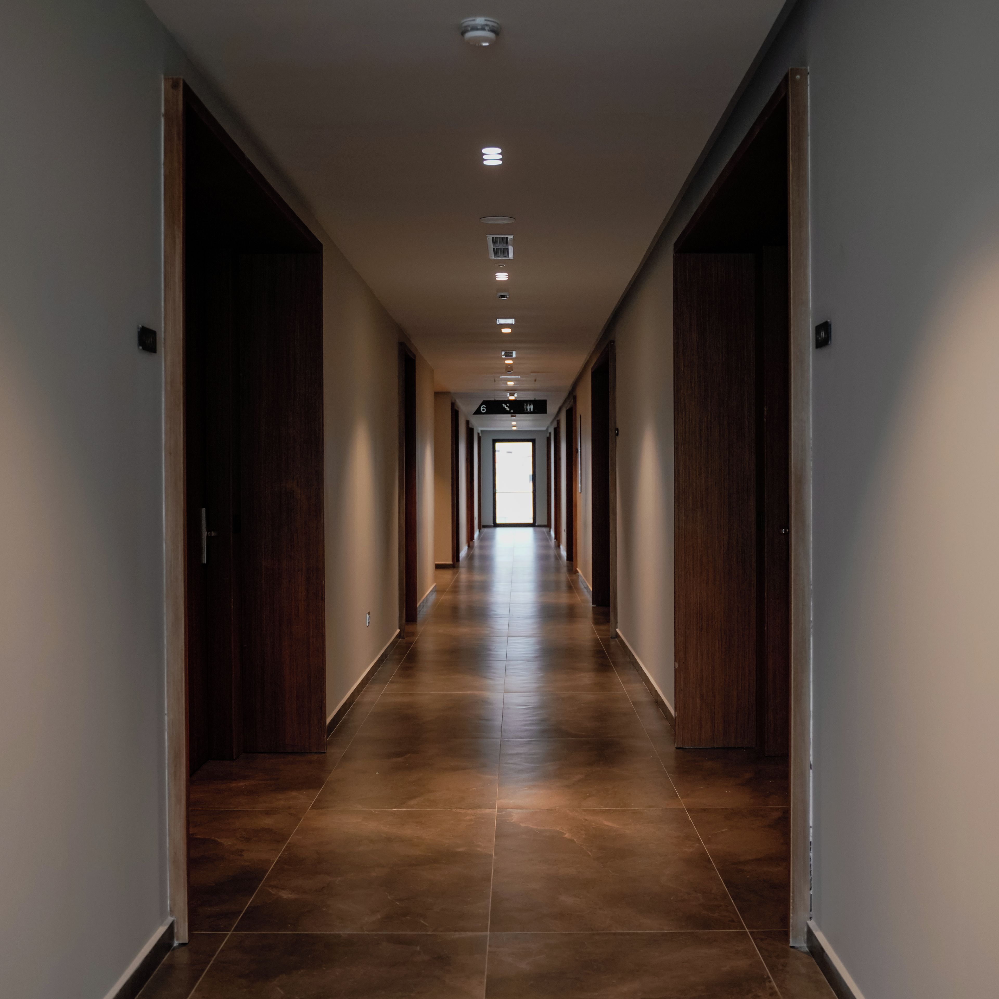 A long, narrow hallway with wooden doors on both sides and a tiled floor.