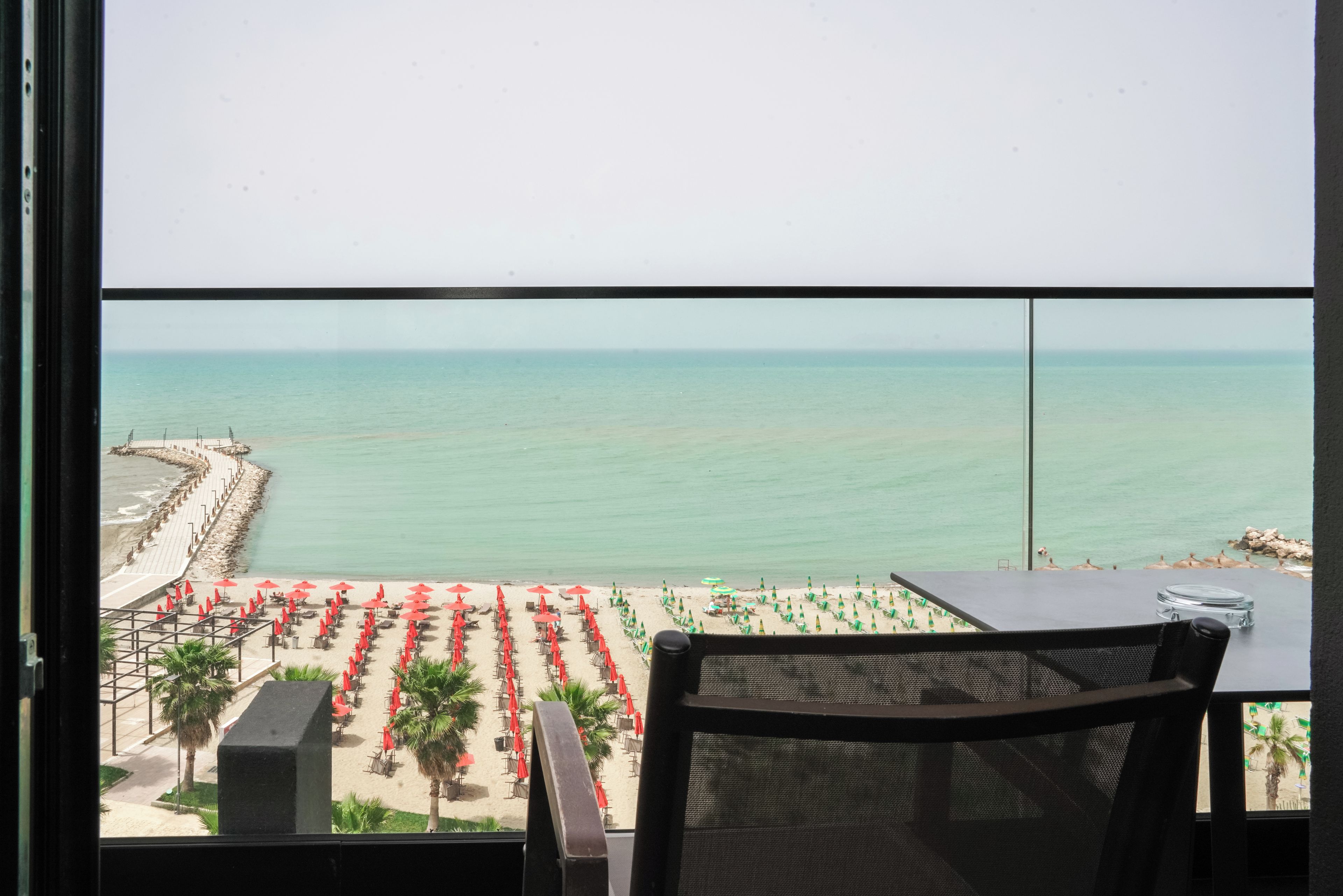 A balcony with a view of a beach with rows of umbrellas and chairs.