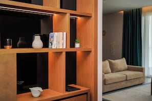 A modern living room with wooden shelves, a beige sofa, and a small potted plant. - Supreme Hotel (Golem)