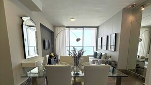 Un salon moderne avec une table à manger en verre, des chaises blanches et une grande fenêtre donnant sur un paysage agréable.