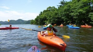 A group of people kayaking on a calm river surrounded by lush greenery. - Sports Pal (Inawashiro)