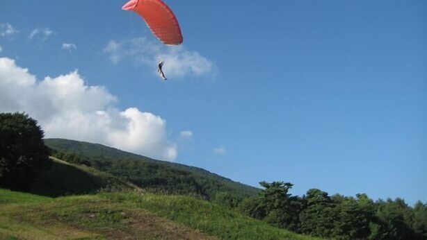 Una persona practica paracaidismo con un paracaídas rojo sobre un paisaje montañoso.
