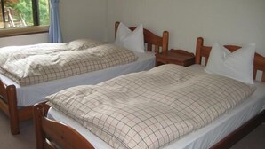 Two single beds with wooden frames and white bedding, a small bedside table, and a window with a view of greenery. - Sports Pal (Inawashiro)