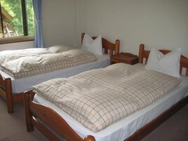 Dos camas individuales con cabeceros de madera y ropa de cama blanca, una mesita de noche pequeña y una ventana con vistas a la vegetación.