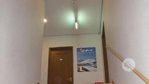 A wooden staircase with a handrail, a door at the top, and a poster on the wall. - Sports Pal (Inawashiro)