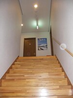 Una escalera de madera con barandilla, una puerta arriba y un cartel en la pared.