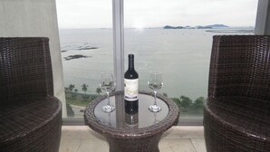 Une table en osier, avec une bouteille de vin Mancura Ethnia et deux verres, offrant une vue sur la côte.