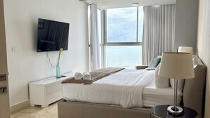 Une chambre d’hôtel moderne dotée d’un grand lit, d’un téléviseur à écran plat, d’une table de chevet avec une lampe et offrant une vue sur la ville par la fenêtre.