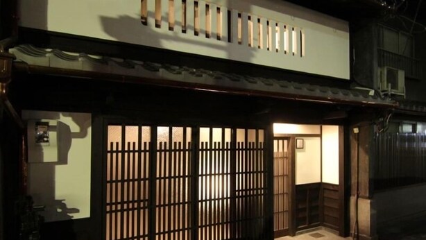 Ein traditionelles japanisches Gebäude mit hölzernem Tor, einem Kachelbelag am Eingang und einer kleinen Veranda.