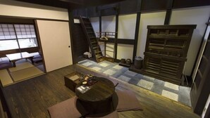 Ein Zimmer mit Tatami-Böden, einem niedrigen Tisch mit Kissen, einer Leiter und einer Schiebetür.