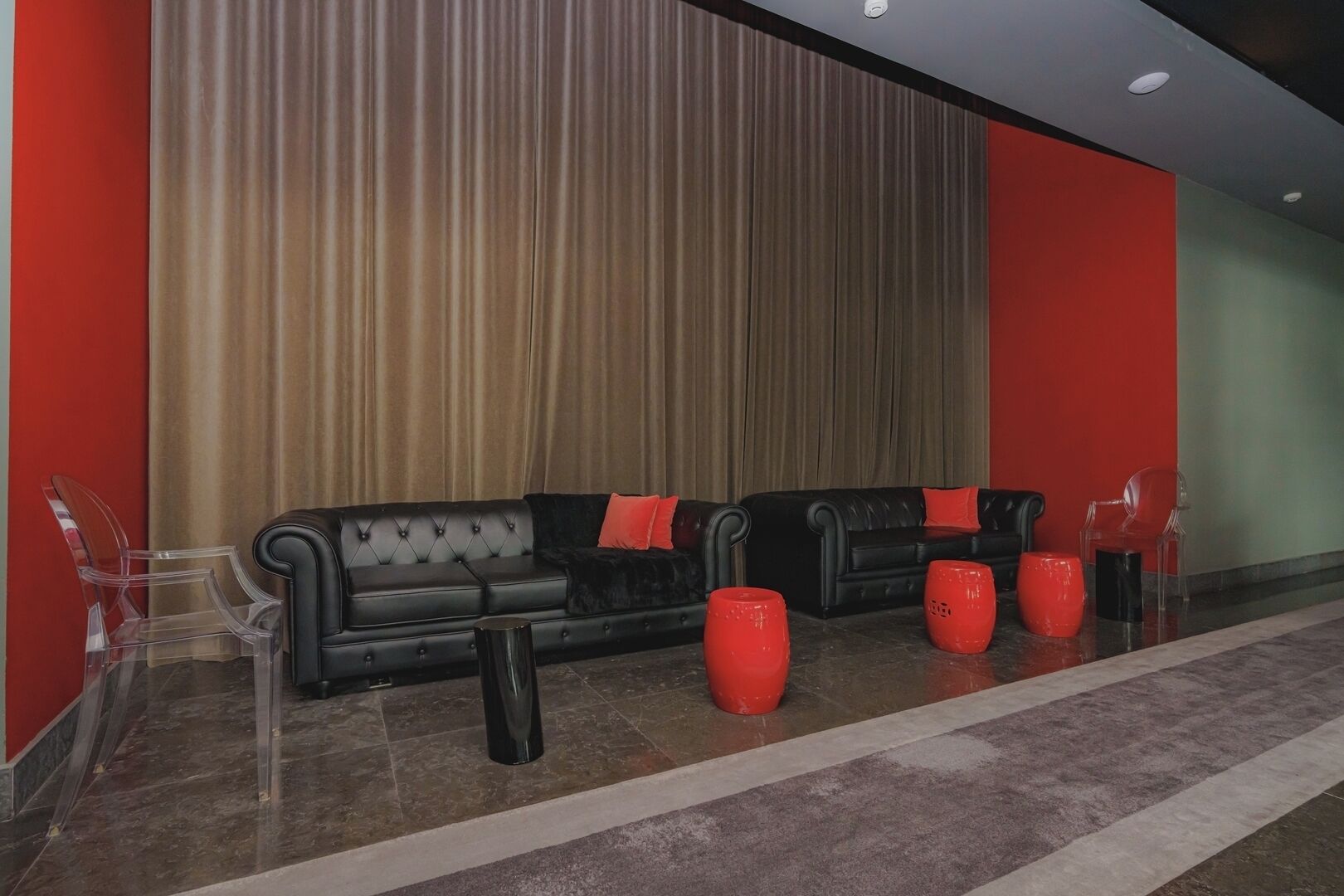 A modern lobby with a black leather sofa, red cushions, and clear plastic chairs.