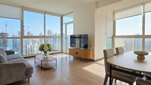 Un salon moderne doté d’une grande fenêtre, d’un canapé, d’une table basse, d’un téléviseur posé sur un meuble en bois et d’une table à manger avec des chaises.