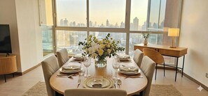A dining area with a table set for four, large windows with a city view, a small side table, and a lamp. - Stunning 3BR with Views, Balcony and Parking (Panamá)