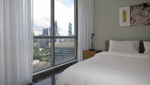 A hotel room with a large window, a bed, a bedside table with a lamp, and a wall with a piece of artwork. - Exclusive and luxury 1BR with balcony in Yoo Panama (Panama City)