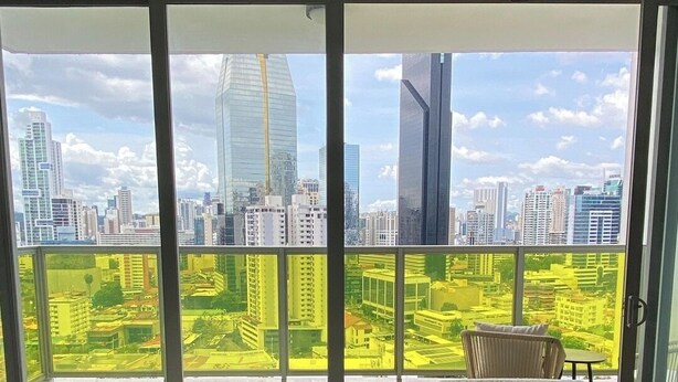 A modern living room with a large sliding glass door leading to a balcony with a city view. - Exclusive and luxury 1BR with balcony in Yoo Panama (Panama City)