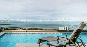 A pool with a glass barrier, two lounge chairs, and a view of the ocean and a bridge. - Stunning 3BR with Views, Balcony and Parking (Panamá)