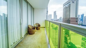 Ein Balkon mit zwei Korbstühlen und einem kleinen Tisch, mit Blick auf eine Stadtlandschaft mit modernen Gebäuden.
