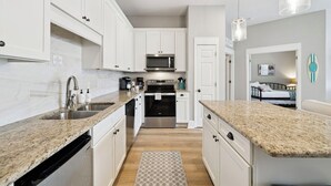 Eine moderne Küche mit weißen Schränken, Granit Arbeitsplatten, Edelstahlgeräten und Pendelleuchten.