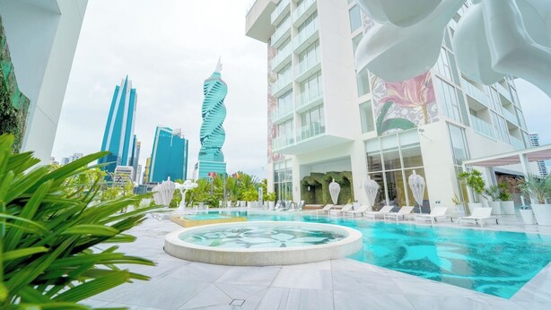 A modern hotel with a pool area, surrounded by greenery and featuring contemporary architecture with a distinctive twisting building in the background. - Exclusive and Luxurious 2BR at Wanders and Yoo (Panama City)