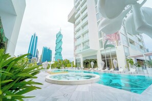 A modern hotel with a pool area, surrounded by greenery and featuring contemporary architecture with a distinctive twisting building in the background. - Exclusive and Luxurious 2BR at Wanders and Yoo (Panama City)