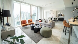 A modern living room with a grey sofa, orange armchairs, and a round ottoman. A dining area with a table and chairs is visible in the background. - Exclusive and Luxurious 2BR at Wanders and Yoo (Panama City)