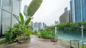 A wooden deck with potted plants and lanterns, overlooking a body of water and a cityscape. - Exclusive and Luxurious 2BR at Wanders and Yoo (Panama City)