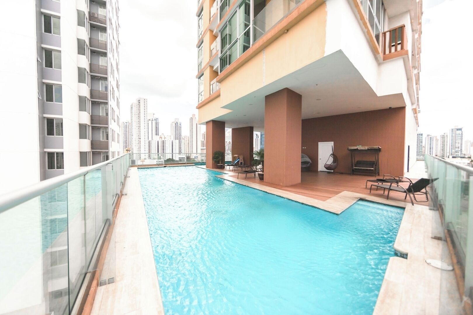 A rooftop pool with a glass balustrade, wooden deck, and lounge chairs.