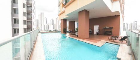 A rooftop pool with a glass balustrade, wooden deck, and lounge chairs.