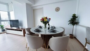 Ein moderner Essbereich mit einem runden Tisch, gedeckt für vier Personen, umgeben von vier Stühlen. Auf dem Tisch steht eine Vase mit Blumen, und an der Wand ist eine Uhr zu sehen.