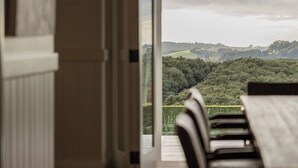 An interior view of a dining area with a table and chairs, a view of the outdoors through a window, and a door leading outside. - Hinterland House (NSW)
