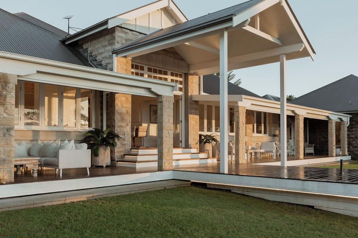 A modern house with a covered patio, stone exterior, and a well-maintained lawn.