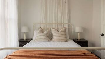 A bed with a metal frame, two bedside tables with lamps, a white curtain, and a brown blanket.