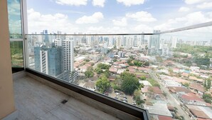 Een hoog appartementencomplex met een ruim balkon, dat uitzicht biedt over de stad, met vele gebouwen en een heldere lucht.