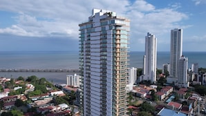Een hoog gebouw met meerdere balkons, omgeven door andere hoge gebouwen en uitzicht op de kust.