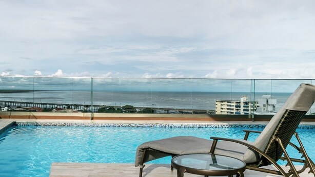 A pool with a glass barrier, lounge chairs, and a view of the ocean and a pier. - Stunning 3BR with Views, Balcony and Parking (Panamá)