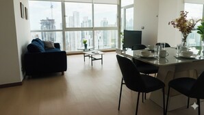A modern living room with a sofa, a dining table with chairs, and a large window offering a city view. - Stunning 3BR with Views, Balcony and Parking (Panamá)