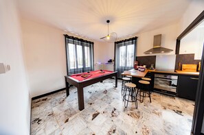 Una habitación con mesa de billar, taburetes de bar, zona de cocina y mesa de comedor.