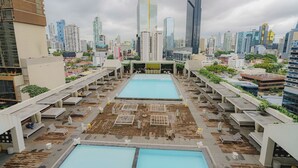 A rooftop pool area with multiple pools and lounge chairs, surrounded by high-rise buildings. - Luxurious 1BR w/ Balcony and Ocean View – Yoo Panama (Panamá)
